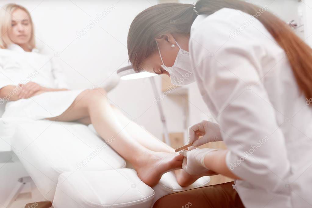 Podiatrist doctor in white making polish procedure for foot.