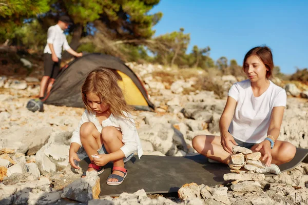 Mamma och liten flicka ställer sten en på stranden. — Stockfoto