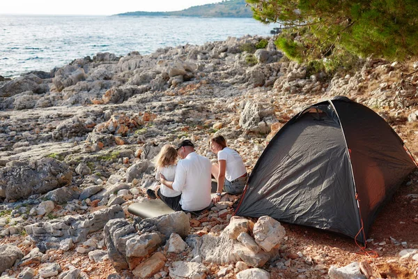 Achteraanzicht van familie, zittend in de buurt van tent op stenen Zeekust. — Stockfoto