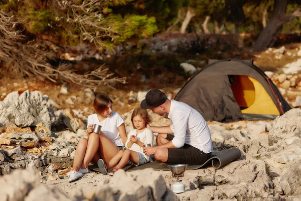 Vriendelijke familie, zittend in de buurt van tent op stenen Zeekust overdag. — Stockfoto