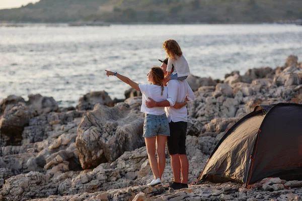 Achteraanzicht van gelukkige jonge ouders, houden handen dochter, staande op een rots strand. — Stockfoto