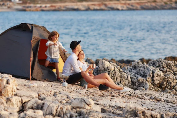 Vriendelijke oprechte familie rust op rotsachtige strand in de buurt van tent. — Stockfoto