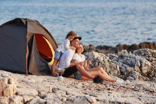 Vriendelijke oprechte familie rust op rotsachtige strand in de buurt van tent. — Stockfoto