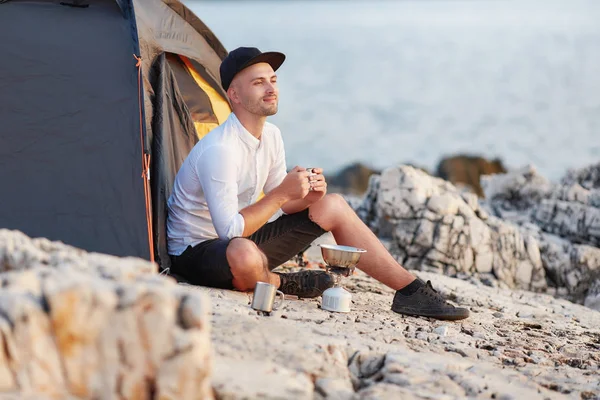 Man zit met een ijzeren cup op rotsachtige kust van zee. — Stockfoto
