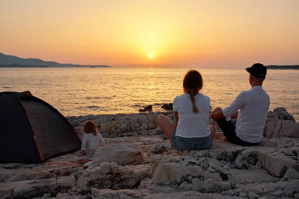 Baksidan på familj, sittande på klippstrand, beundra solnedgången över havet. — Stockfoto