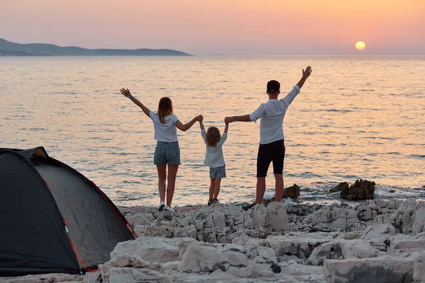 Achteraanzicht van zoete jonge gezin, permanent met open handen op rots strand. — Stockfoto