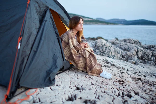Meisje zit onder tenten, verpakt in plaid, kop geurige thee houden. — Stockfoto