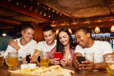 Smartphone kullanarak ve bira ve atıştırmalıkların bulunduğu eğlenerek mutlu arkadaşlar.