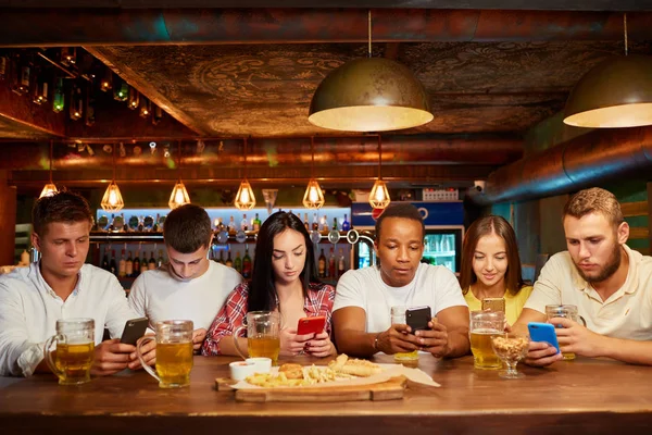 Group of six friends with serious facial expression, sitting with smartphones, drinking beer at bar. — Stock Image Group of six friends with serious facial expression, sitting with smartphones, drinking beer at bar. Stock Photo