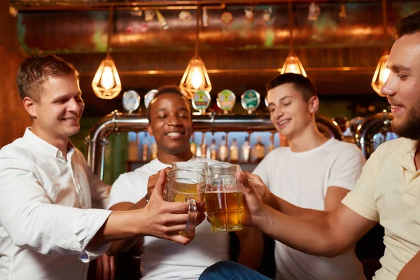 Four friends raising glasses of beer and celebrating their friendship in cozy pub. — Stock Image Four friends raising glasses of beer and celebrating their friendship in cozy pub. Royalty Free Stock Images
