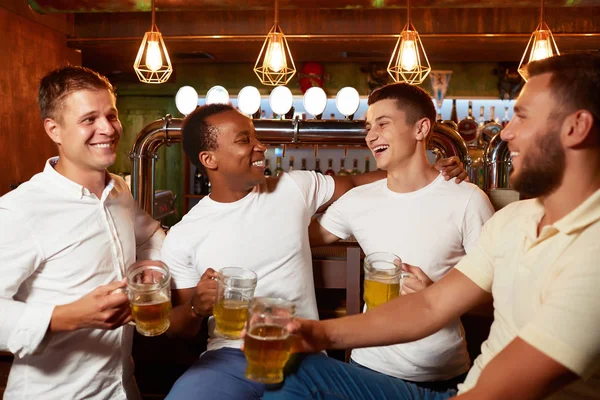 Company of four handsome men holding glass of beer, smiling and embracing. — Stock Image Company of four handsome men holding glass of beer, smiling and embracing. Royalty Free Stock Images