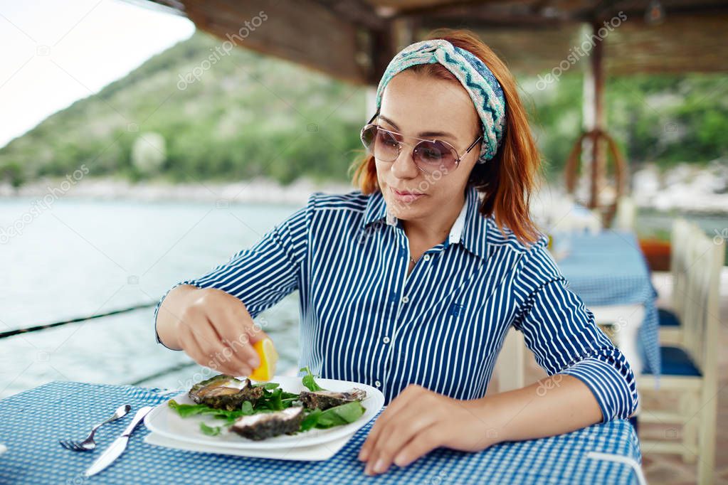 Woman eating a delicacy oyster, close-up outdoor restaurant