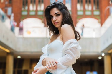 Sevimli genç esmer kamera Valencia'da binanın arka plan bulanık üzerinde dururken bakarak gündelik kıyafeti