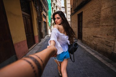 Arkadan görünüşü tanınmaz halde kişinin elini tutarak ve Valencia İspanya dar sokakta yürürken rahat kıyafet içinde oldukça genç bayan