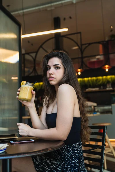 Lezzetli smoothie bardak tutan ve güzel kafede masada otururken kameraya bakarak güzel genç esmer yan görünüm