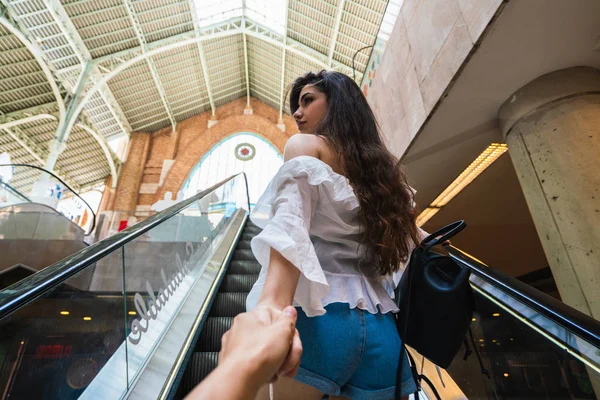 Arkadan görünüşü gündelik kıyafeti Valencia Alışveriş merkezinde yürüyen merdiven üzerinde kırpma kişi ve önde gelen yolu el dayanabiliyor genç bayan
