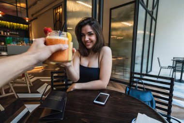 Çekici genç kadın gülümseyerek ve yuvarlak Cafe tablo ve prangalara gözlük tanınmaz arkadaşıyla lezzetli güler yüzlü, otururken kameraya bakıyor