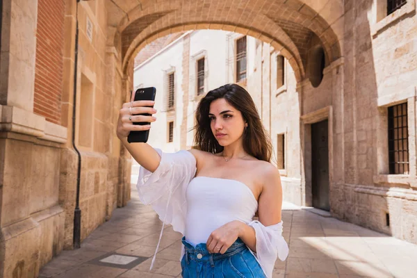 Smartphone ve alma selfie dururken Valencia sokakta güneşli günde tutan güzel genç esmer