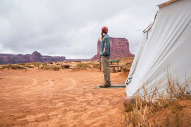 Elleri ceplerinde tutmak ve uzak Monument Valley, Utah bulutlu gün çadır yakın dururken seyir şık kıyafeti tanınmaz sakallı erkek yan görünüm