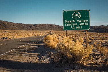 Büyük yeşil tabela yakınındaki mavi gökyüzü arka plan üzerinde Death Valley California uzun Asfaltlı yol görünümünü