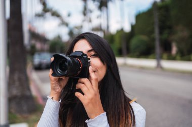 Modern fotoğraf makinesi kullanarak ve kamera Los Angeles, Kaliforniya'nın Caddesi'nin arka plan bulanık üzerinde dururken bakarak Genç esmer
