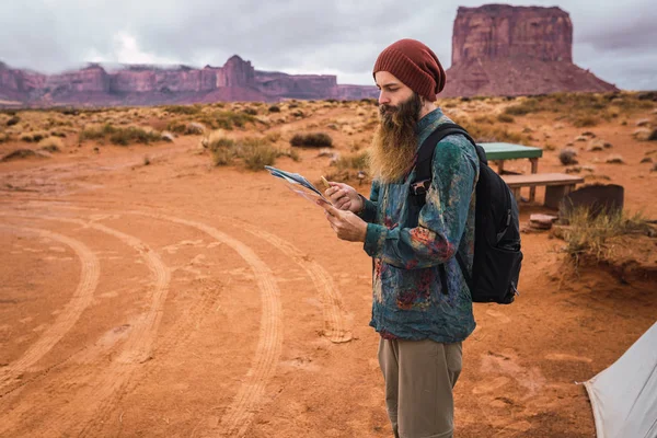 Side view of bearded man with backpack looking at map and compass while standing in Monument Valley, Utah