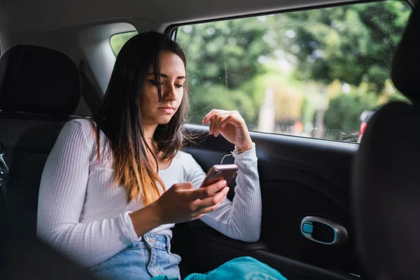 可爱的年轻女士在时尚的装备浏览智能手机 而旅行通过洛杉矶的现代汽车后座 — 图库照片