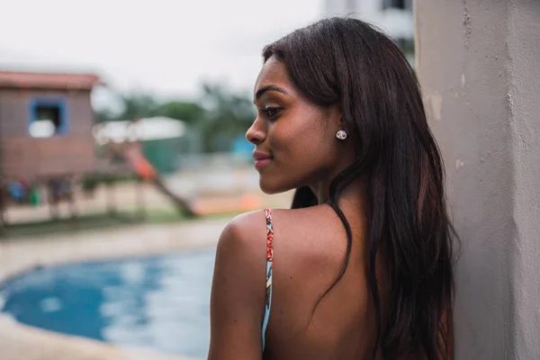 Back view of sensual flirty African American woman in dress looking over shoulder standing in poolside