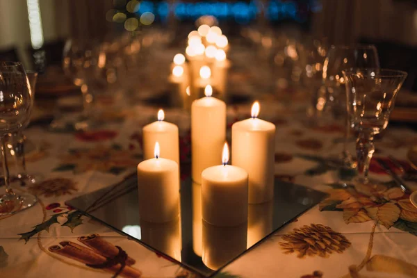 Composition of white candles burning brightly on table with shiny glassware prepared for holiday dinner
