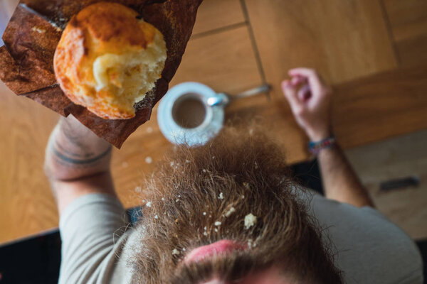 Crop man from above eating cupcake with crumbs on beard standing at table