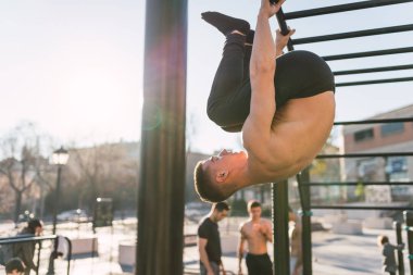 Genç sportif gömleksiz adam üzerinde çene barlar açık spor salonunda kadar güneşli bir günde eğitim yan görünüm