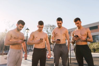 Genç sportif gömleksiz erkekler arka plan bulanık Park'ta cep telefonlarında tarama