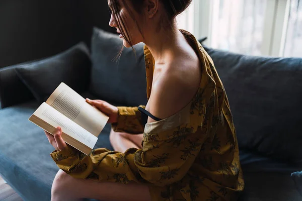 Mujer joven con libro sentado en el sofá —  Fotos de Stock