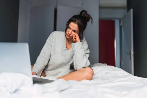 Yatağa dizüstü bilgisayar kullanan genç üzgün kadın — Stok fotoğraf