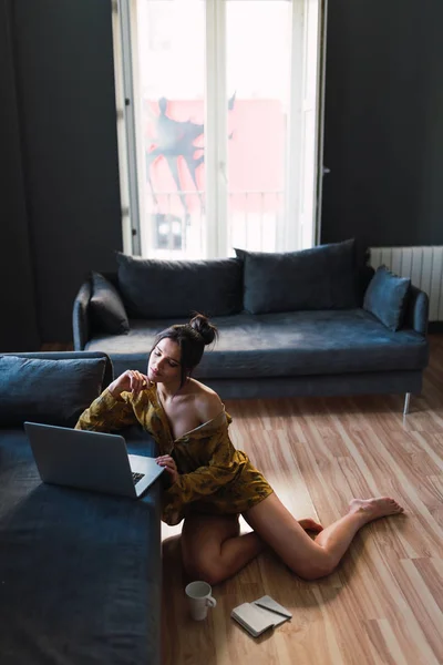 Young slim woman using laptop near sofa and cup on floor — Stock Photo, Image