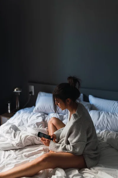 Jovem mulher com smartphone sentado na cama — Fotografia de Stock