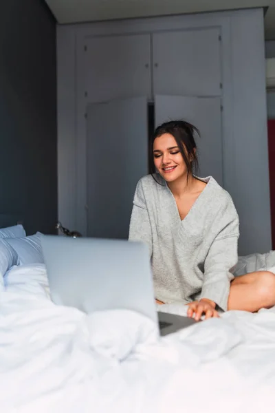 Jovem sorrindo mulher usando laptop na cama — Fotografia de Stock