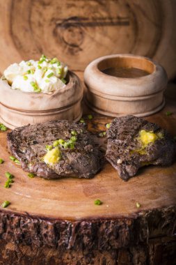 Biftek, patates püresi ve erimiş tereyağlı sos ile servis edilir.
