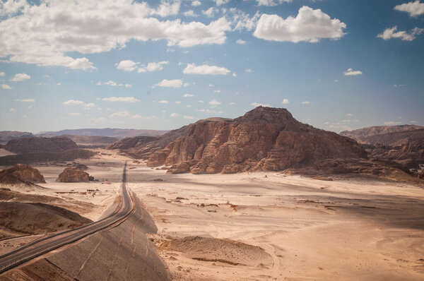 Desert landscape with blue sky and sun with road,sand and mountains