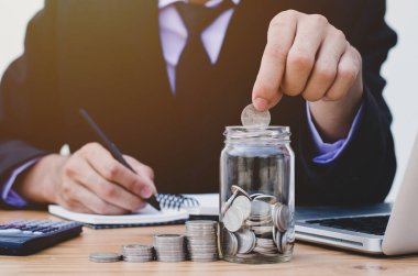Para biriktirmek için para biriktiren iş hesapları, madeni kavramların olduğu cam bir kavanoza para koyuyor..