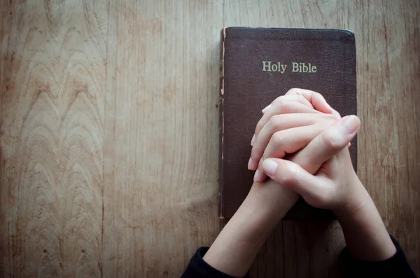 Pray in the Morning, Woman praying with hands together, Woman praying while holding Bible And some of the blurred text in Bible