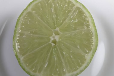Beyaz tabakta dilimlenmiş yeşil limon. İzole edilmiş. Vejetaryen yemeği.