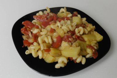 Beyaz arka planda izole edilmiş siyah bir tabakta haşlanmış sebzeli makarna.