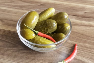 Ahşap arka planda cam kasede kırmızı biberli salatalık turşusu.,