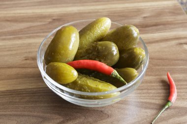 Ahşap arka planda cam kasede kırmızı biberli salatalık turşusu.,