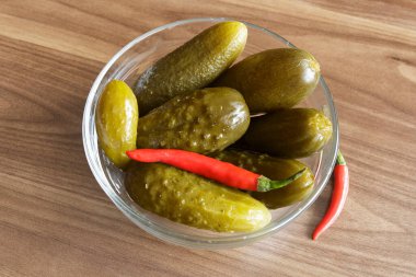 Ahşap arka planda cam kasede kırmızı biberli salatalık turşusu.,