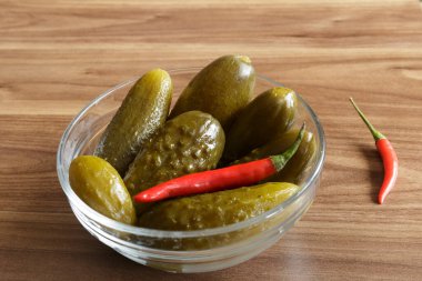 Ahşap arka planda cam kasede kırmızı biberli salatalık turşusu.,