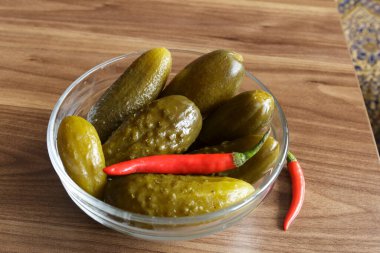 Ahşap arka planda cam kasede kırmızı biberli salatalık turşusu.,