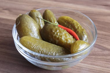 Ahşap zemin üzerinde kırmızı biber yığını olan yeşil salatalık turşusu, lezzetli atıştırmalık konsepti, vegan yemeği..