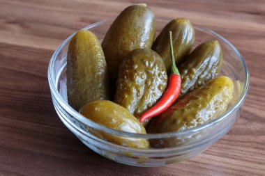 Ahşap zemin üzerinde kırmızı biber yığını olan yeşil salatalık turşusu, lezzetli atıştırmalık konsepti, vegan yemeği..